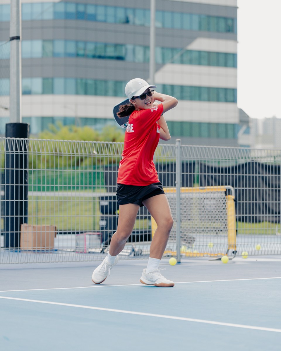 Smiling junior player in a red shirt following through on a backhand